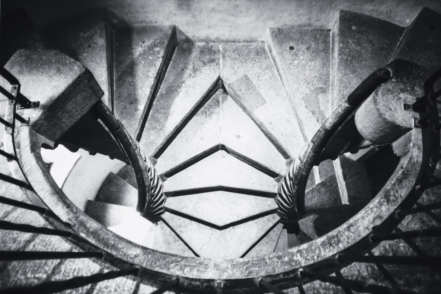 A high-angle view shows a double spiral staircase with stone steps and ornate railings.