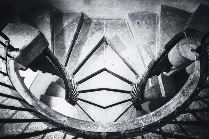 A high-angle view shows a double spiral staircase with stone steps and ornate railings.