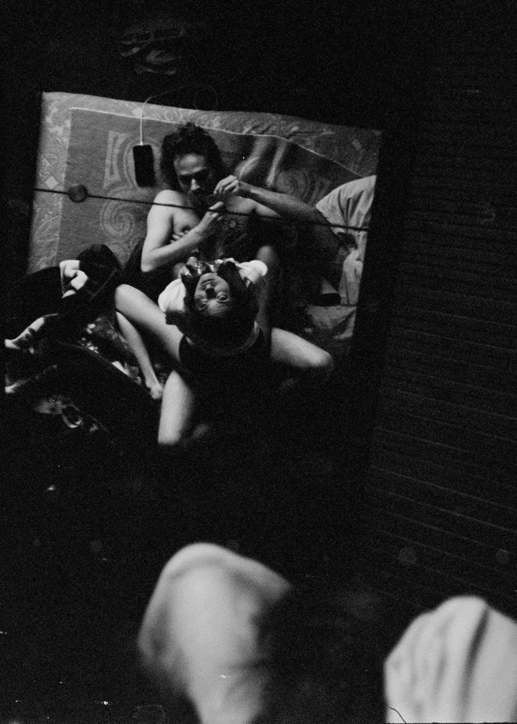 A man and a woman are lying on a bed, with the woman looking up at the camera.
