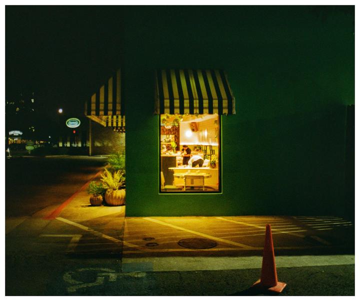 A brightly lit storefront window with a striped awning is visible at night, with a traffic cone in the foreground.