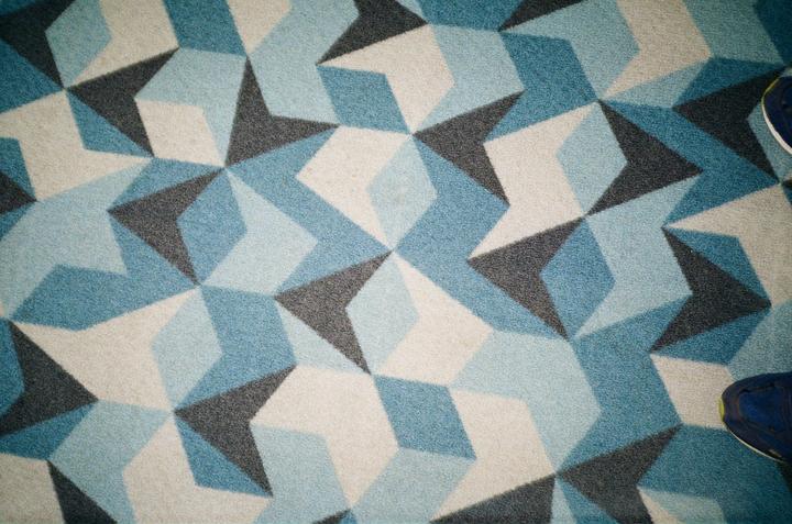 A blue shoe is visible on a patterned carpet with geometric shapes in shades of blue, gray, and white.