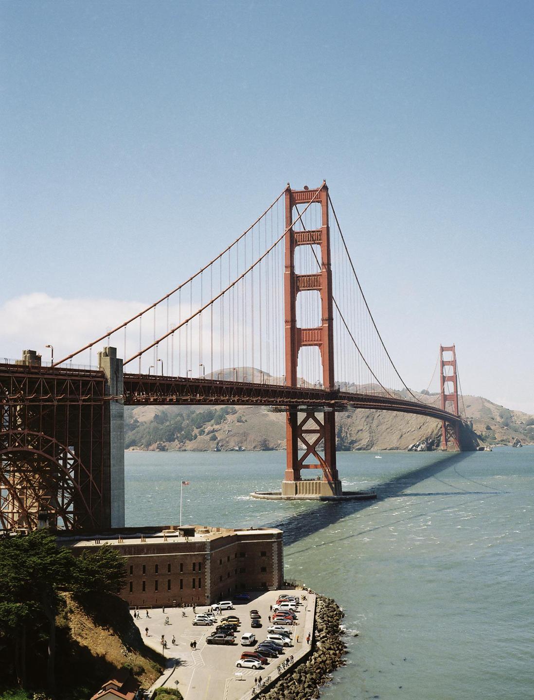The Golden Gate Bridge spans across a body of water with a building and parking lot in the foreground.
