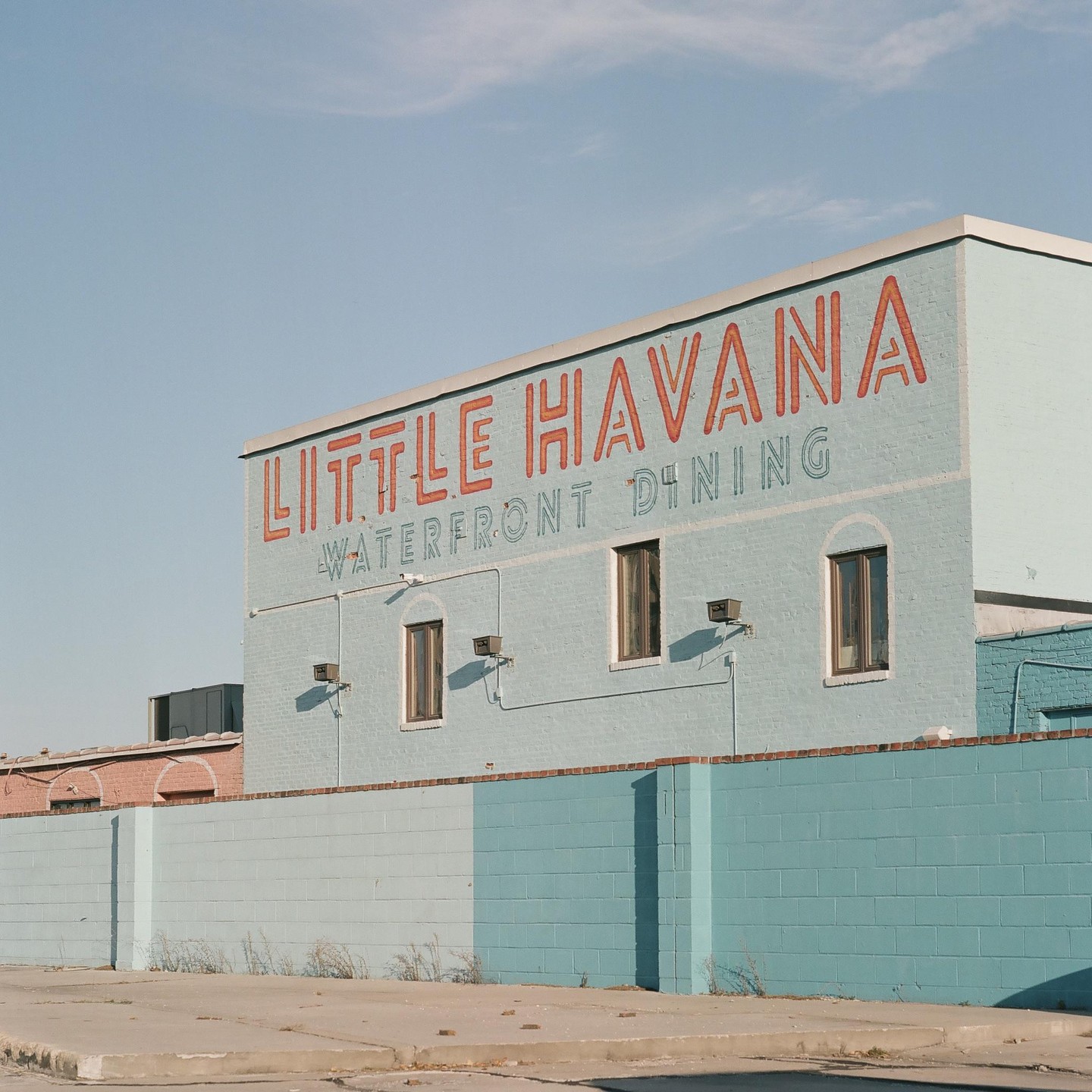 A light blue building with "Little Havana Waterfront Dining" painted on its side stands under a clear sky.