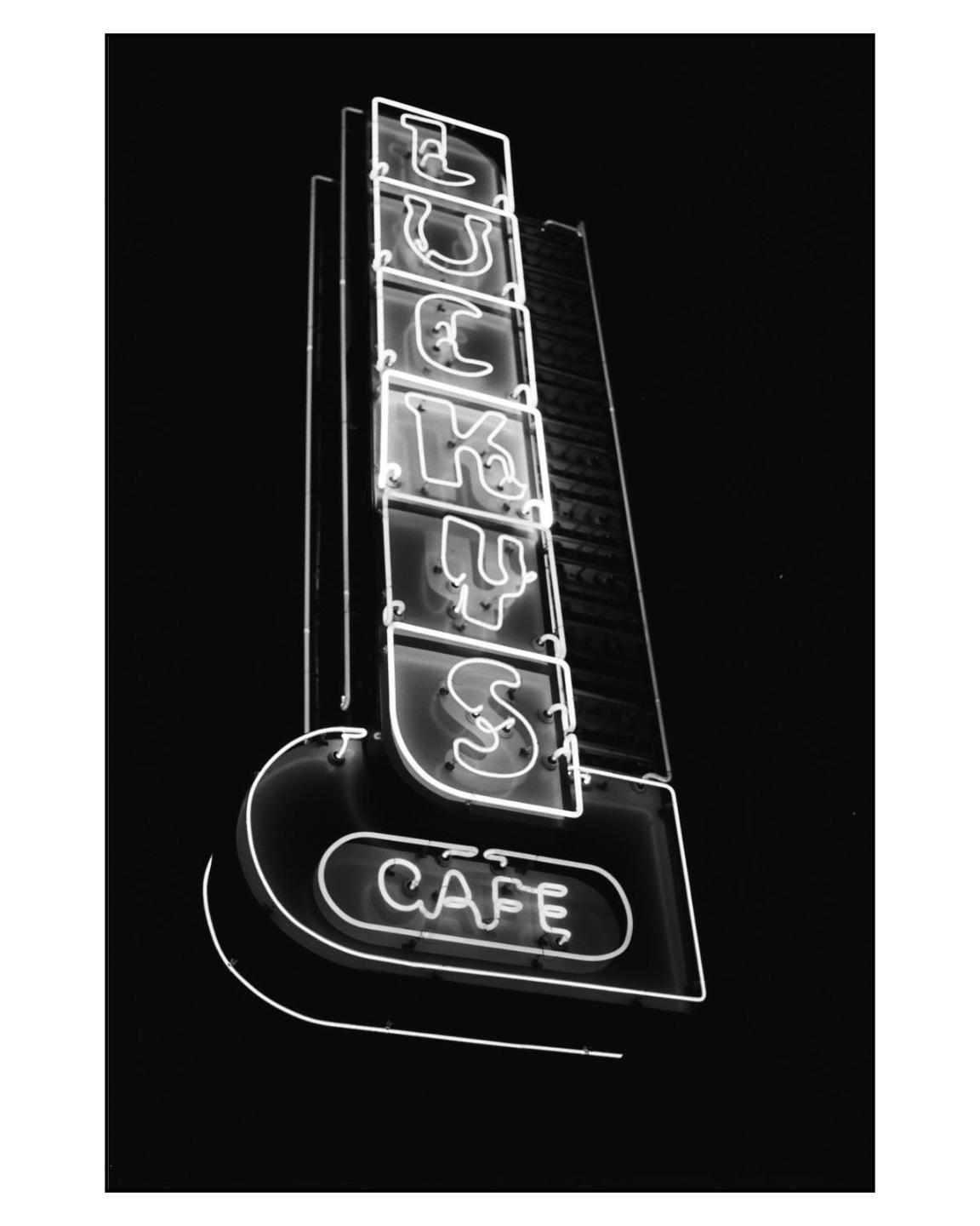 A neon sign for "Lucky's Cafe" is illuminated against a dark background.