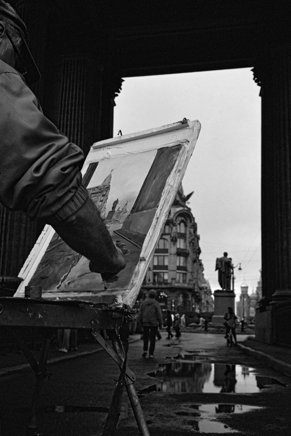 A person paints a street scene on an easel, with a statue and buildings visible in the background.