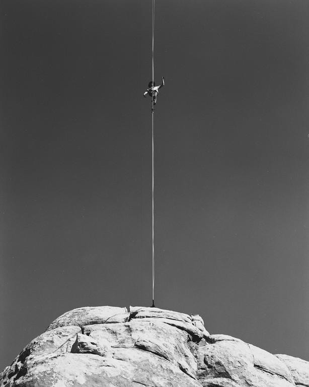 A man walks a tightrope high above a rocky mountain.