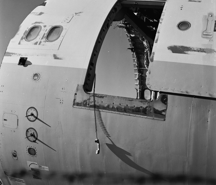A telephone receiver hangs from a cord on the side of a damaged airplane fuselage.