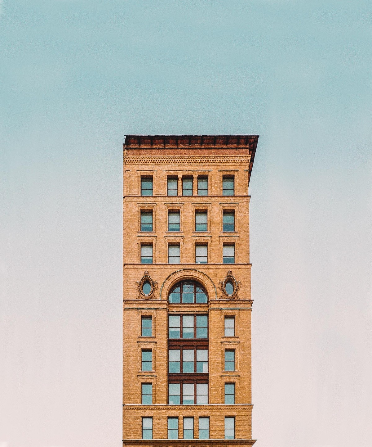 A tall brick building with many windows stands against a clear sky.