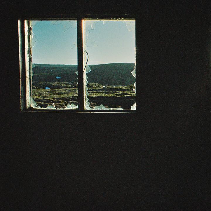 A broken window looks out onto a vast, mossy landscape under a clear sky.