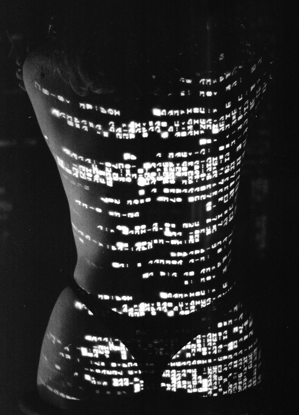 The back of a woman is illuminated by projected text.