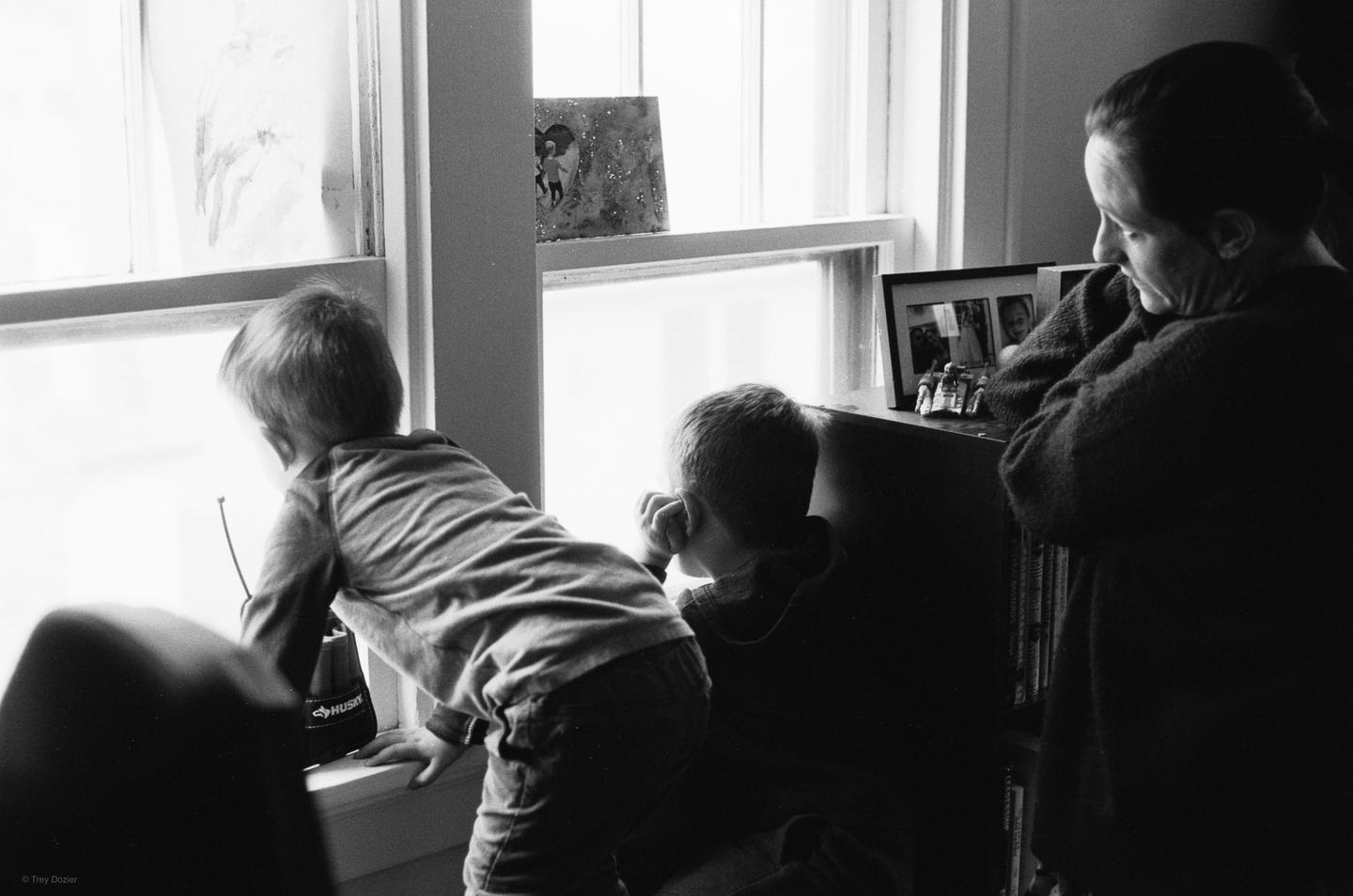 Two children look out a window while a woman stands nearby, all in black and white.