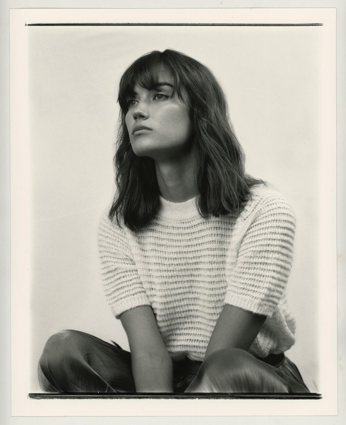 A woman with bangs and long hair sits looking to the left in a studio portrait.