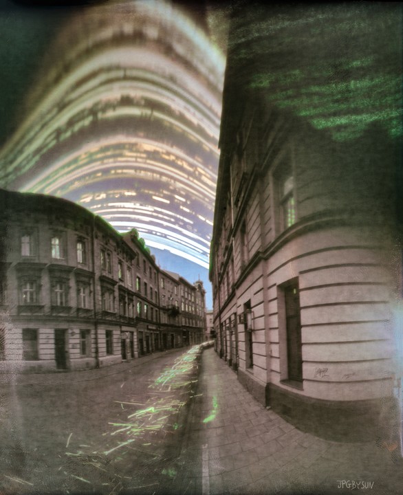 A street in Krakow is lined with buildings under a sky filled with light trails.