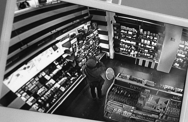 A person stands in a store aisle, viewed from above on a surveillance monitor.