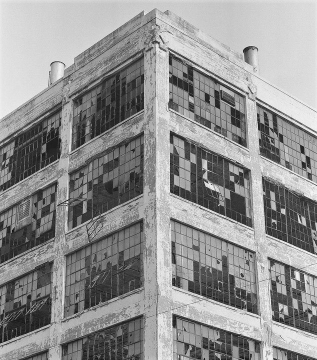 An old industrial building with many broken windows is shown from a low angle.