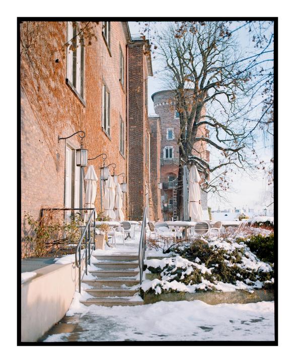 A snow-covered outdoor patio with tables and umbrellas is next to a brick building with ivy.