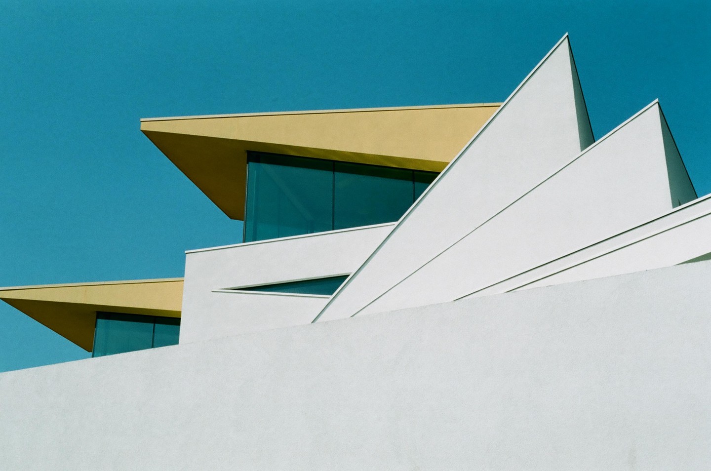 A modern building with sharp angles and a yellow roof is set against a clear blue sky.