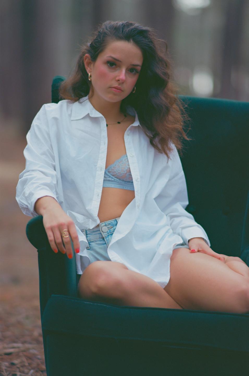 A woman with long hair and a white shirt is sitting on a green armchair outdoors.