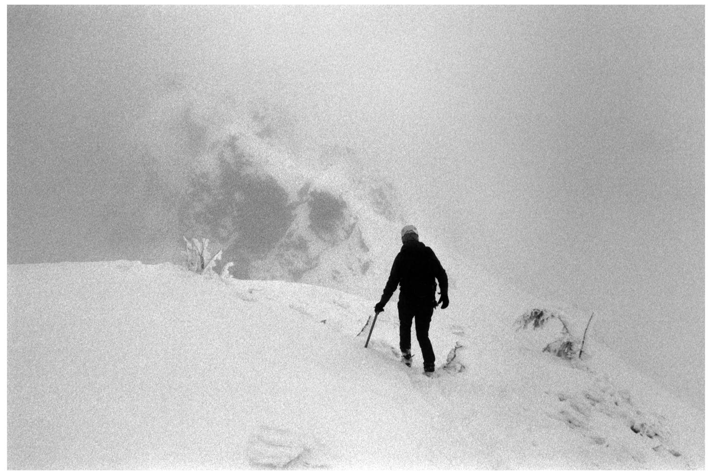 A person walks through a snowy landscape with an ice axe in hand.