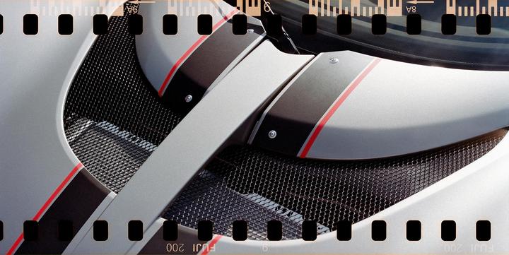 A close-up shot shows the details of a silver car with black and red stripes and a black mesh grill.