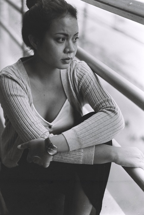 A woman with her hair tied up sits with her arms crossed, looking to the right of the frame.