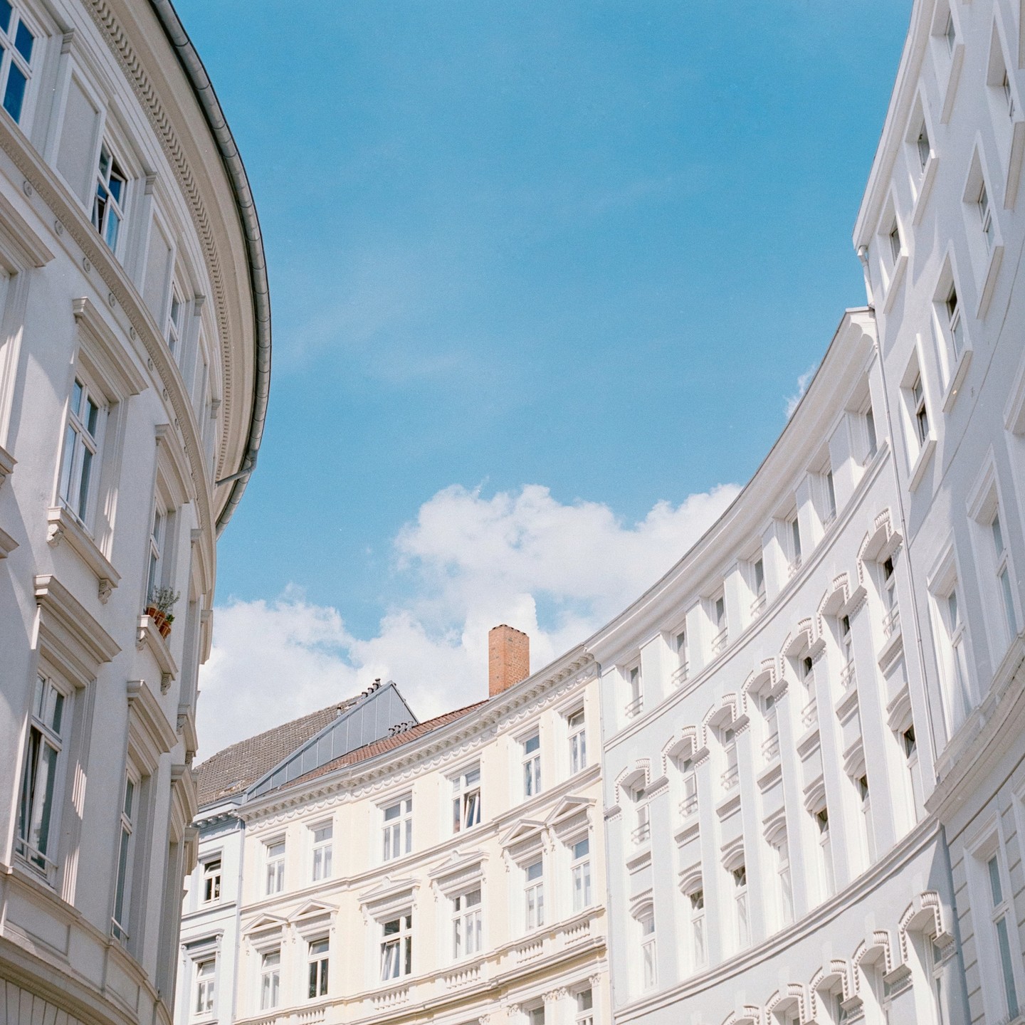 Two curved white buildings with many windows frame a bright blue sky with white clouds.