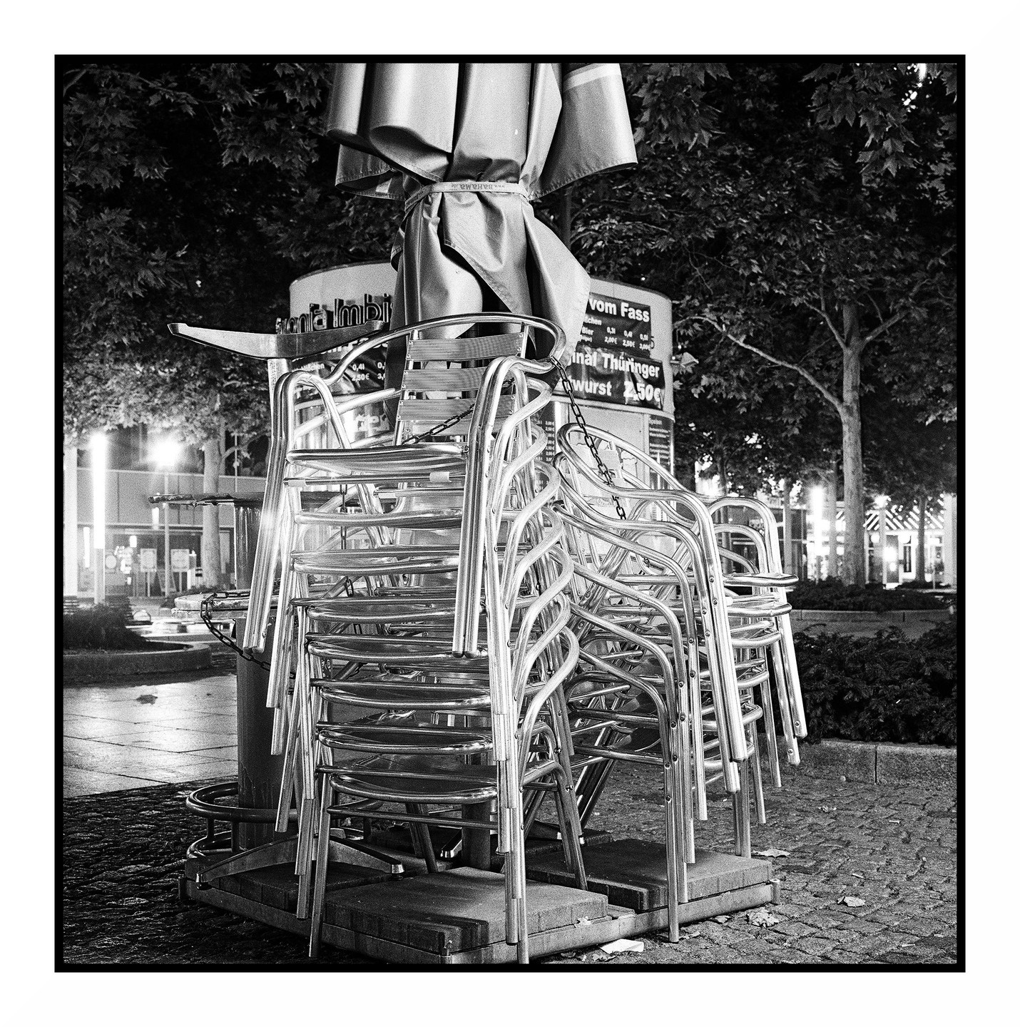 Stacked chairs and a closed umbrella are visible at night outside a restaurant.