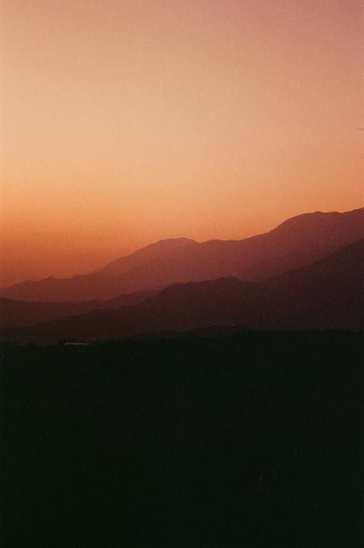 A landscape of layered mountains is silhouetted against a vibrant sunset sky.