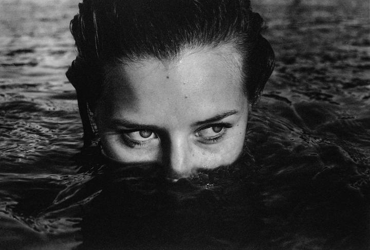 A woman's face is partially submerged in water, with only her eyes and forehead visible.