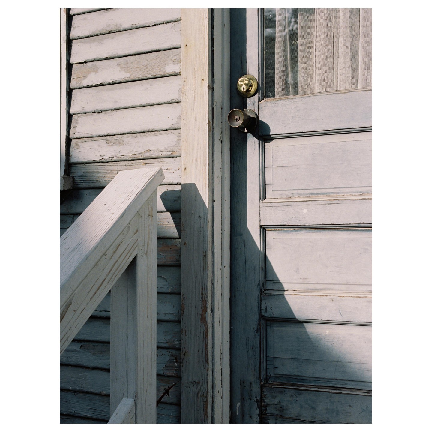 A weathered wooden door and siding are illuminated by sunlight, casting a shadow on the door.