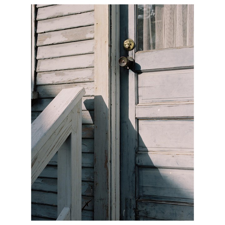 A weathered wooden door and siding are illuminated by sunlight, casting a shadow on the door.