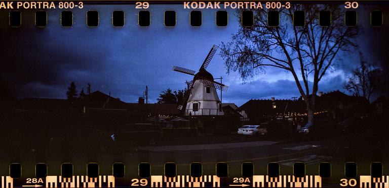 A white windmill stands under a dark blue sky with bare trees and buildings in the background.