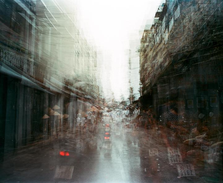 A busy street market is captured with multiple exposures, creating a sense of movement and a hazy atmosphere.