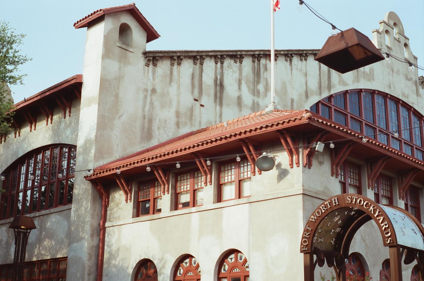 A building with a red tile roof and arched windows is visible under a clear sky.