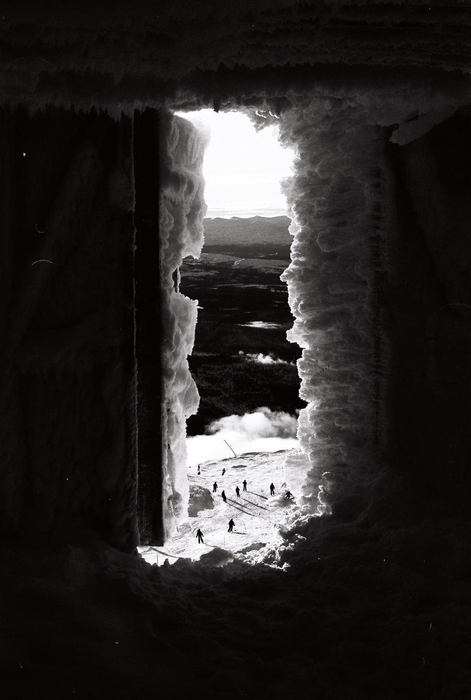 A group of skiers is visible on a snowy mountain slope through a snow-covered opening.