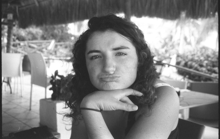 A woman with curly hair rests her chin on her hand and makes a pouting face.