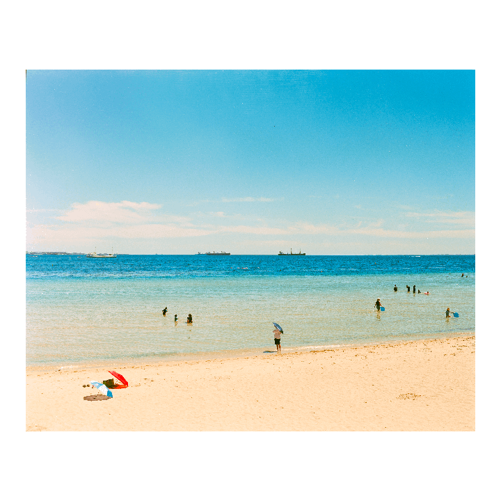 A wide shot shows a beach with people in the water and two umbrellas on the sand.