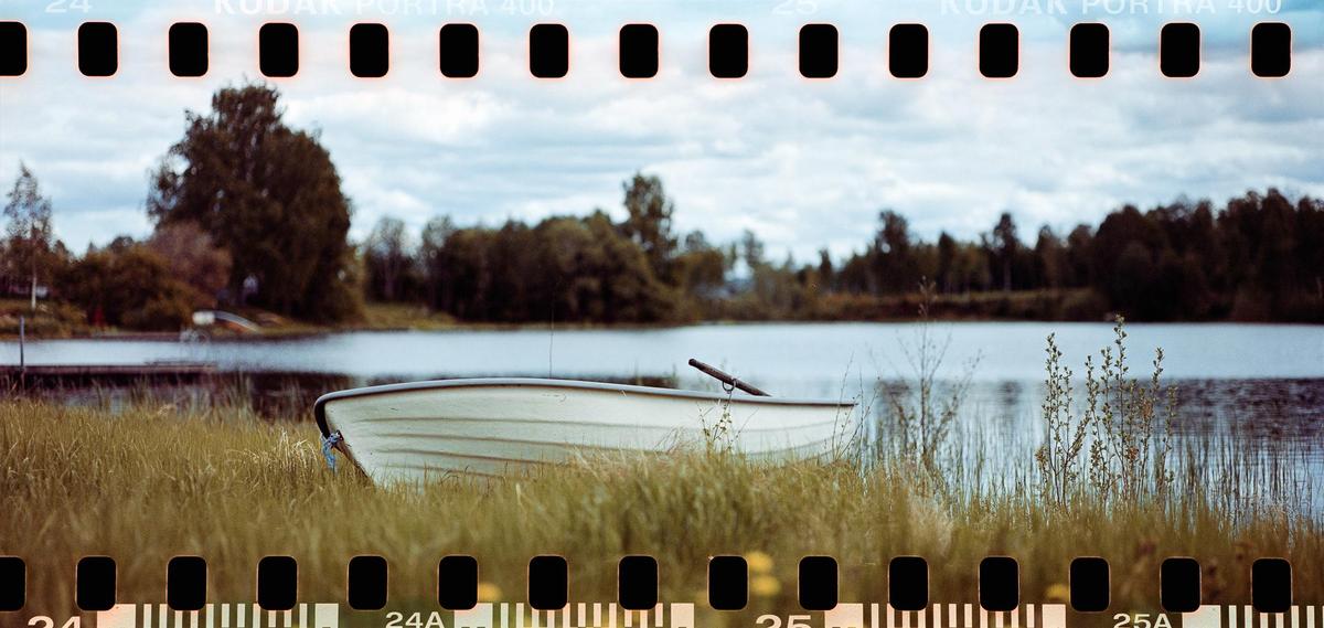 A small boat rests on a grassy bank beside a lake with trees in the background.