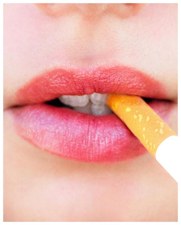A woman's red lips hold a cigarette filter in her mouth.