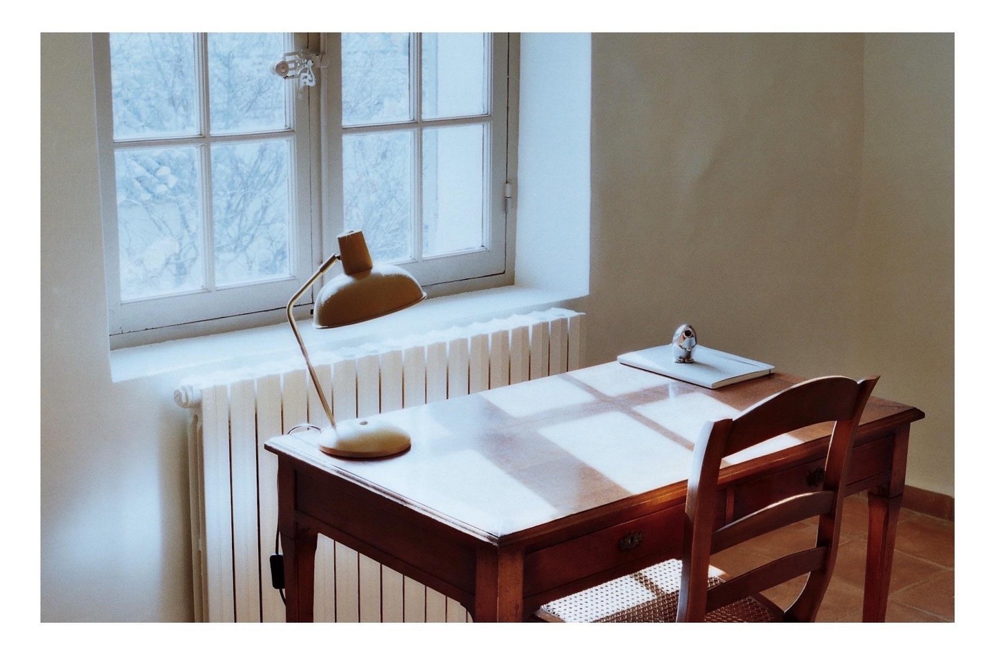 A desk with a lamp and a chair sits in front of a window with a radiator below it.