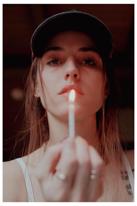 A woman wearing a baseball cap holds a lit matchstick in front of her face.
