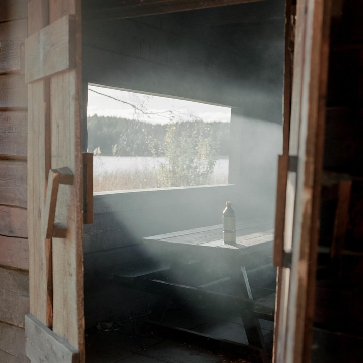 Sunlight streams through a window into a smoky wooden hut, illuminating a bottle on a picnic table.