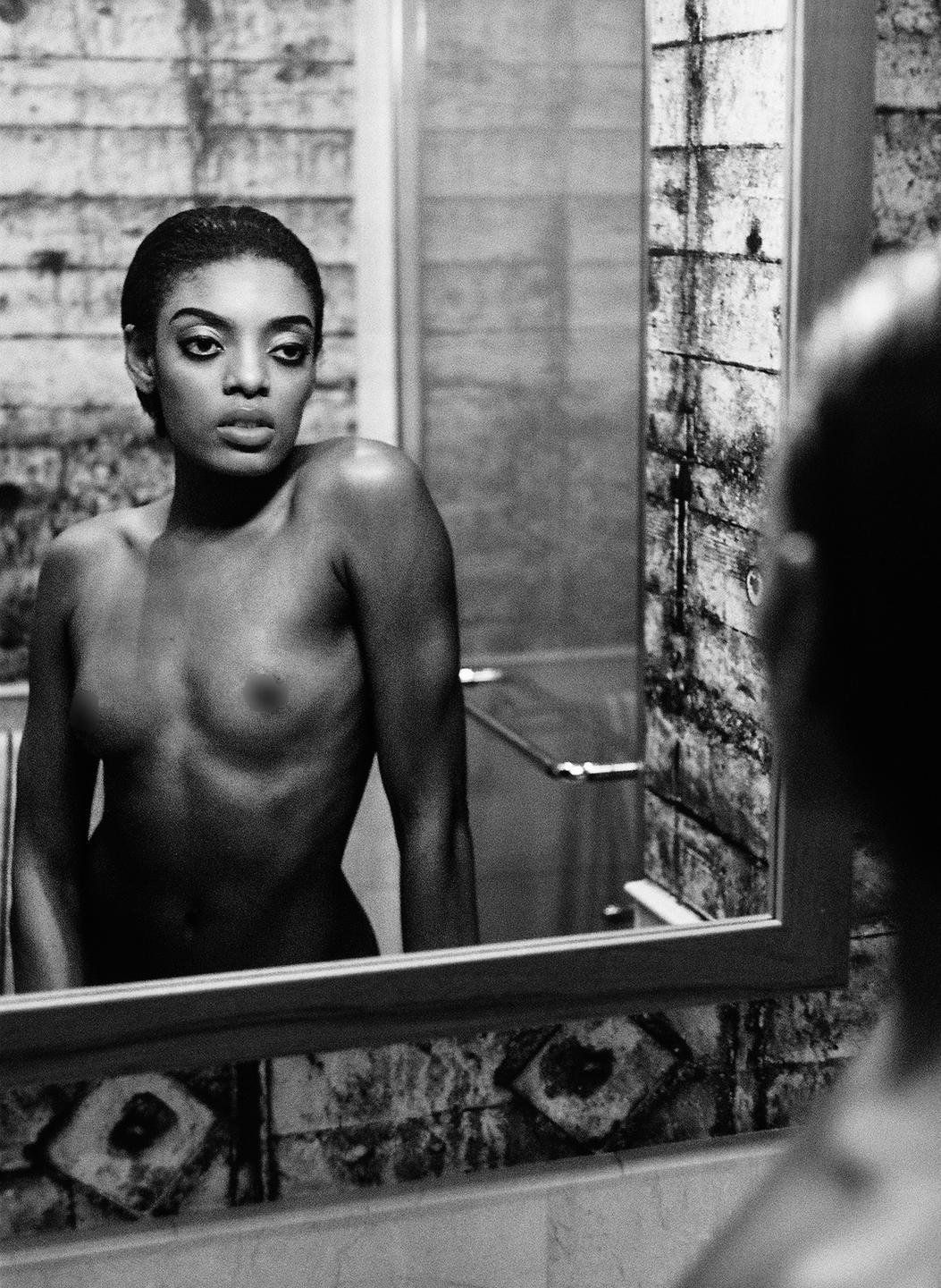 A woman looks at her reflection in a mirror in a bathroom.