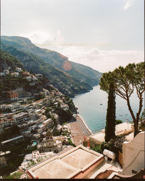 A hillside town with many buildings and a beach is visible next to a body of water with mountains in the background.