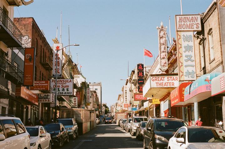 A street in Chinatown is lined with parked cars and buildings with many signs in English and Chinese.