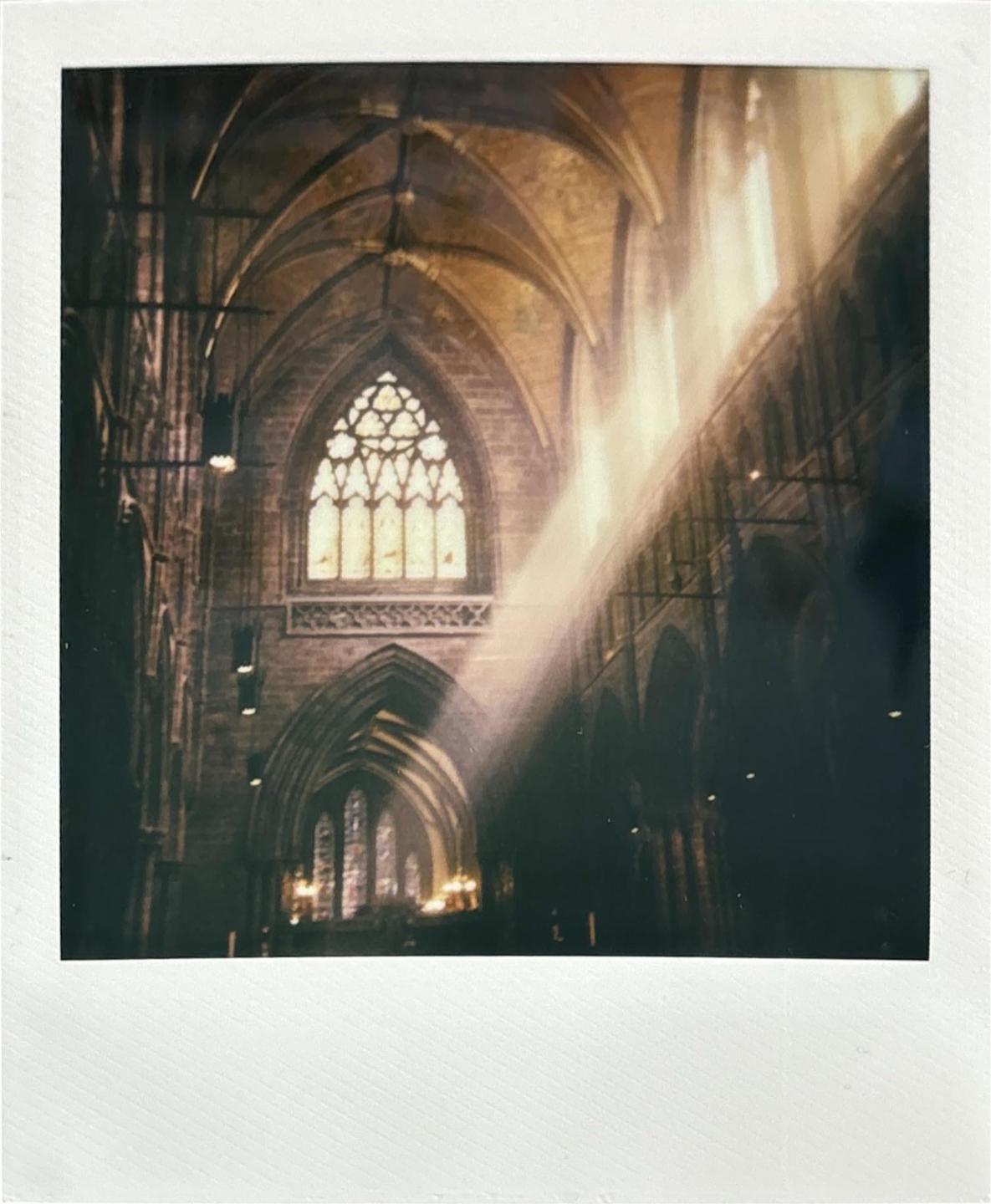 Sunlight streams through a large stained glass window into a gothic cathedral.