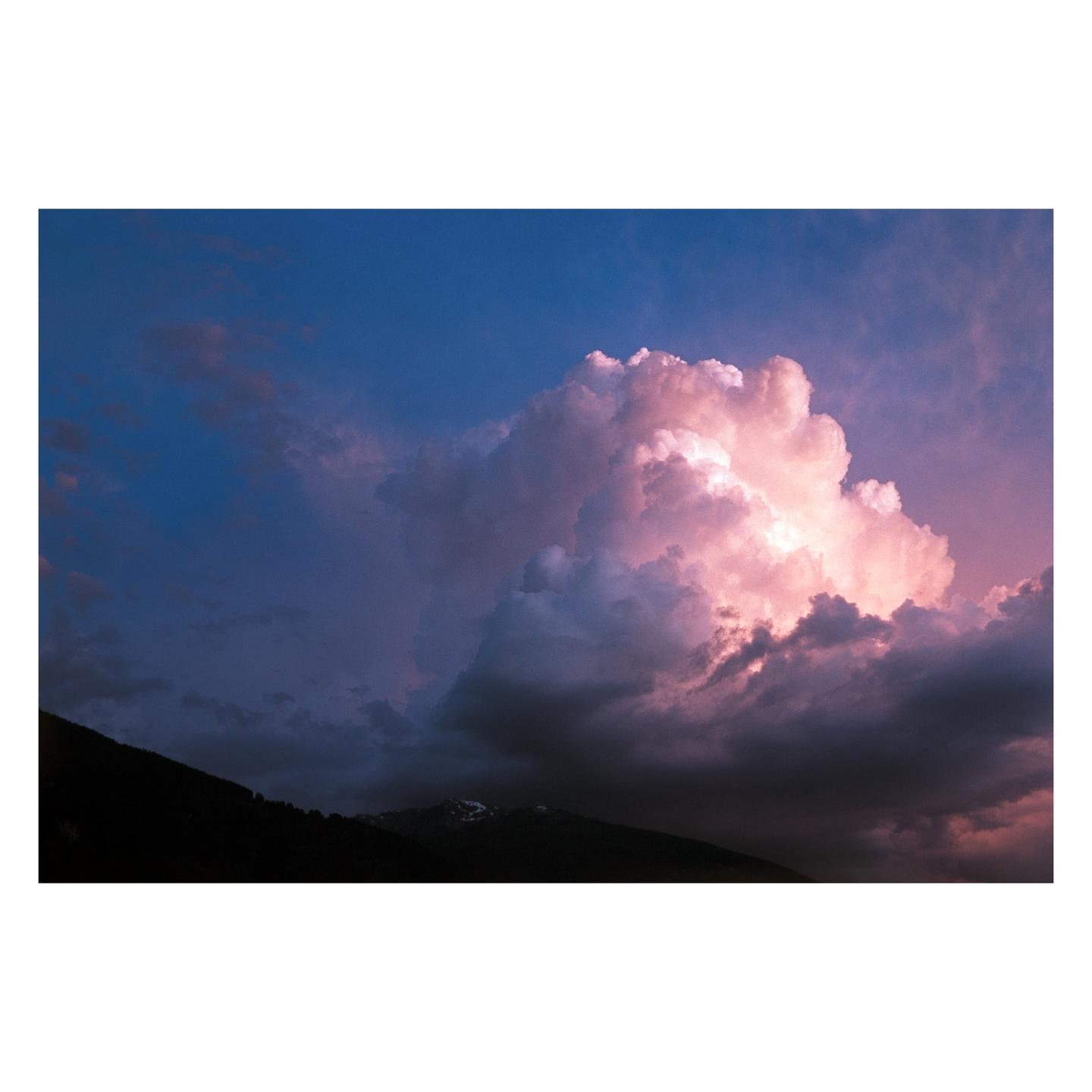 A large, bright pink cloud dominates the sky above dark mountains.