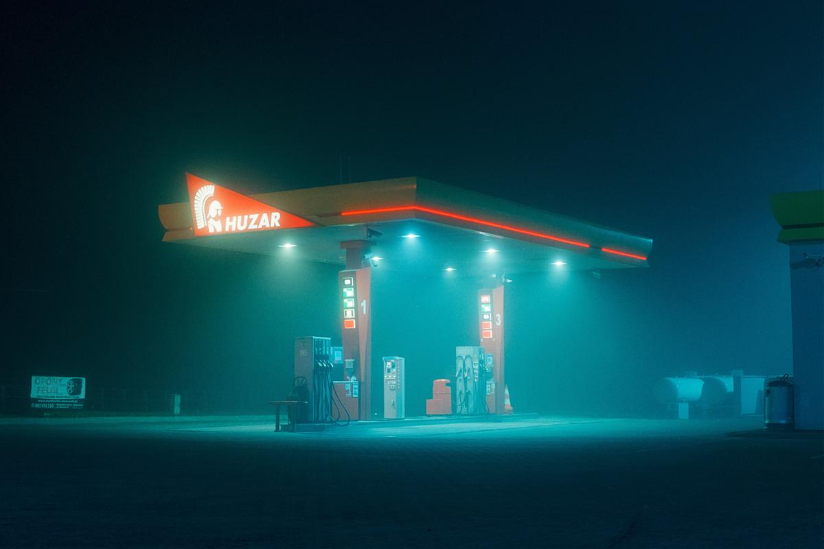 A gas station with red and blue lights illuminates a foggy night.