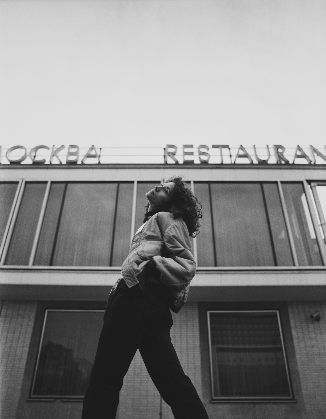 A woman with curly hair looks up at a building with a restaurant sign.