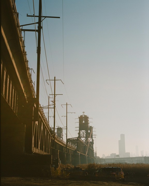 A long bridge with power lines runs alongside a hazy cityscape with tall buildings in the distance.